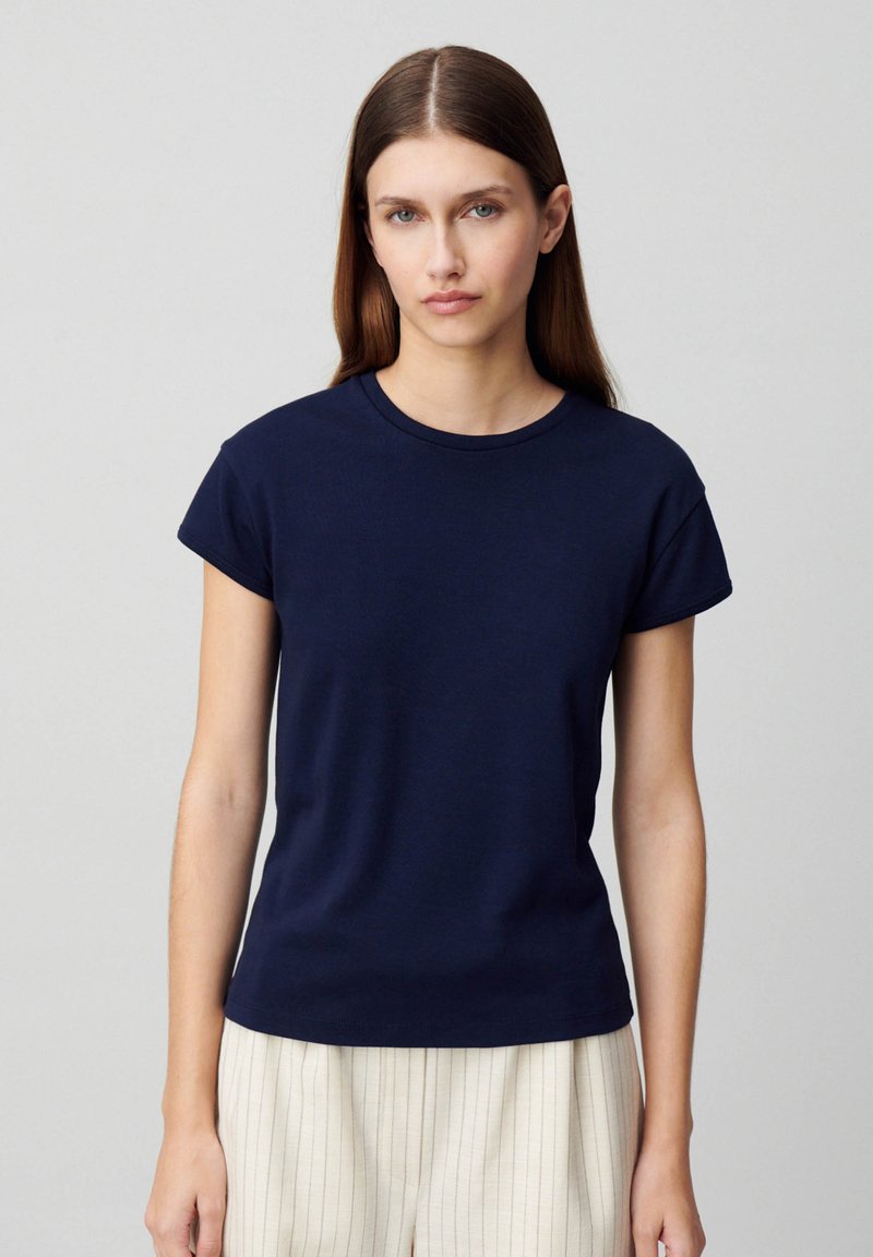 T-shirt blu navy a maniche corte con scollo rotondo, texture morbida e vestibilità leggermente rilassata, abbinata a pantaloni a righe chiare.