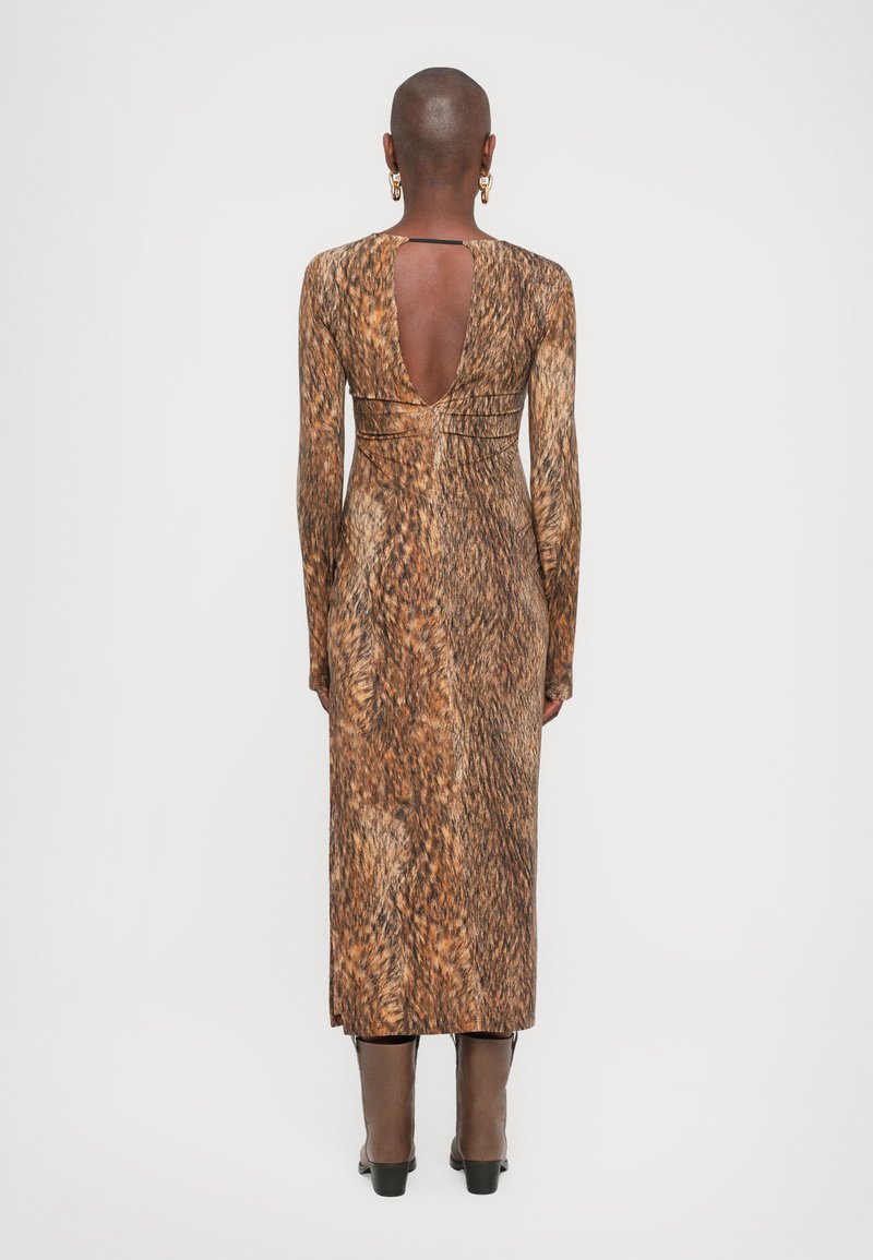 Maxiklänning i djurmönster med långa ärmar, öppen rygg och figurnära design. Bruna toner med textilstruktur. Buren med stövlar som går upp till knäna.