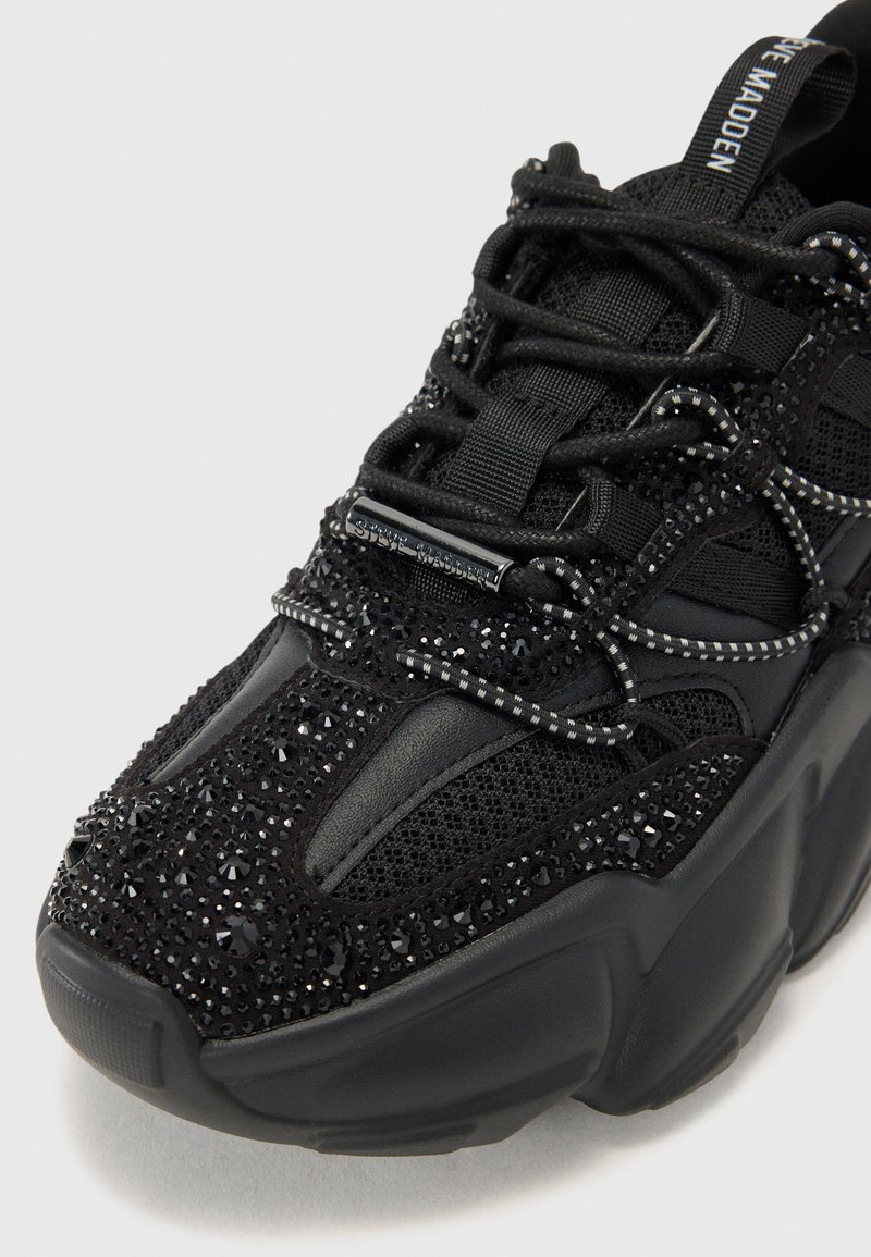 Baskets noires chunky en maille et tissu texturé avec des embellissements scintillants, des lacets accentués et une semelle épaisse pour le soutien.
