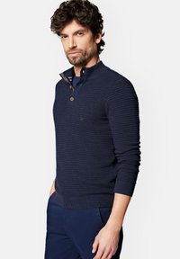 Granatowy, teksturowany sweter z połową zapięcia na guziki oraz akcentami w postaci pasków na kołnierzyku. Dopasowane rękawy i dół z subtelnym detalem logo.