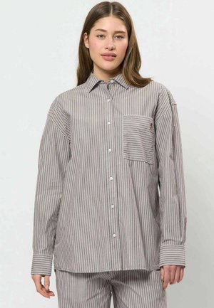 Jeune femme portant une chemise ample à manches longues boutonnée avec de fines rayures verticales et horizontales et un pantalon assorti rayé.