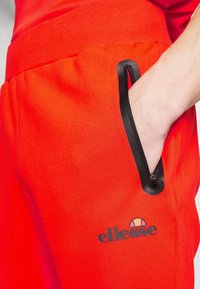 Röda sweatpants med en ribbad midja, som har en dragkedjeficka kantad i svart och en liten svart logotyp, mjukt tygmaterial.