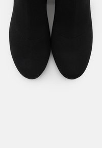Chaussures slip-on noires en tricot avec une texture lisse, un bout arrondi et un design de tige sans couture. Les semelles sont plates et minimalistes.