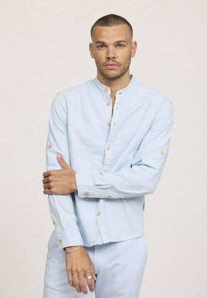 Chemise bleu clair à boutons avec col officier, dotée de boutons en bois et de manches longues, portée avec une coupe décontractée. Texture en coton lisse.