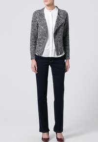 Grijze gebreide motorjack met een rits aan de voorkant, witte blouse eronder, gecombineerd met donkerblauwe jeans en bordeauxrode schoenen. Eenvoudig ontwerp, textuur zichtbaar.