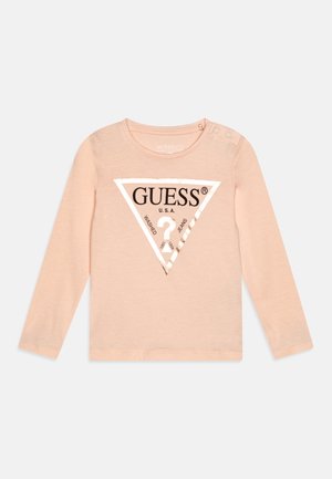 Suéter melocotón de manga larga con un logo metálico en forma de triángulo en el frente, con botones a presión en el hombro para facilitar el vestirse.