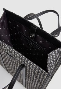 Textureradtyg tote bag med ett geometriskt mönster i svart och vitt, med läderremmar och en slät svart foder med tryckt logotyp.