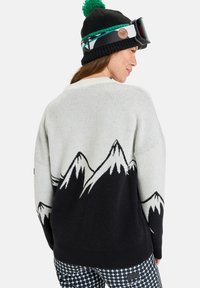 Light grey knit sweater featuring black mountain graphic and cream accents. Paired with a black beanie with a green pom-pom.
