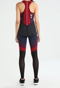 Sportowy top bez rękawów w burgundowym kolorze z siateczkową dolną częścią, zestawiony z legginsami w kolorze czarnym, burgundowym i granatowym z kątowym blokowaniem kolorów i czarnymi akcentami.
