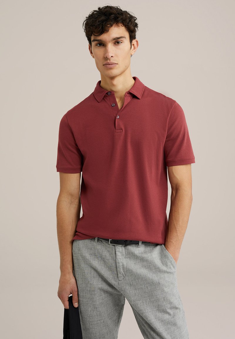 Camiseta polo burdeos con cuello y tapeta de tres botones; mangas cortas; combinada con pantalones gris claro; textura suave.
