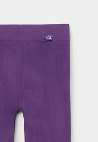 Paarse geribde legging met een klein label met de tekst "clz" aan de tailleband. De stof lijkt rekbaar en textuur te hebben.