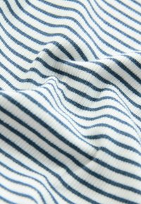 Weißer Stoff mit gleichmäßig verteilten schmalen marineblauen horizontalen Streifen, der eine strukturierte Rippung und weiche Falten zeigt.