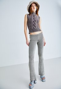 Conjunto de punto que incluye un top sin mangas tipo cuello alto con patrón de trenzas, pantalones acampanados a rayas y sandalias de plataforma azul claro con un tacón grueso.