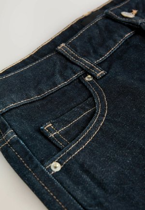 Mörkblå denimjeans med kontrasterande tan-färgade sömmar, som har en framficka, metallknapp och en slät yta.