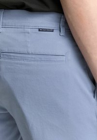 Lichtblauwe broek met een gladde textuur, met een achterzak en een klein zwart label met "TOM TAILOR" nabij de tailleband.