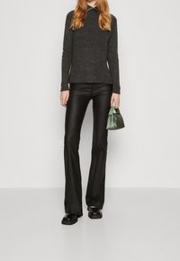 Maglione grigio a coste con collo alto fasullo, abbinato a pantaloni neri in pelle a zampa d'elefante. Tiene una piccola borsa verde. Scarpe slip-on nere.