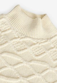 Pull en tricot beige clair avec un col côtelé haut et des motifs en diamant texturés sur l'ensemble du tissu. Apparence douce et volumineuse.
