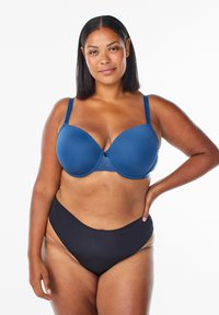 Blauwe naadloze bh met kantdetail en beugel, voorzien van verstelbare bandjes. Draagt met hoge zwarte slipjes. Glad textuur.