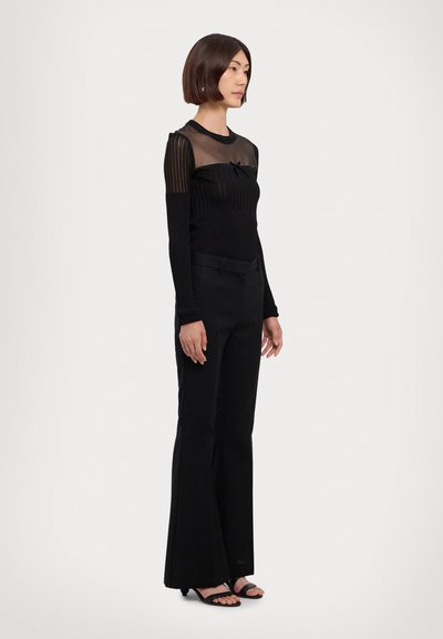 Top lung cu mânecă lungă, negru, având un design transparent, cu dungi. Asortat cu pantaloni evazați negri și sandale plate negre. O ținută ușoară și versatilă.