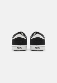 Zapatillas de ante negro con acentos blancos y suelas de goma. Presentan cuellos acolchados y un logo bordado en el talón. Diseño clásico de corte bajo.