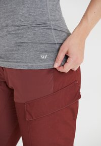 Grå tajt topp med en subtil logotyp, i kombination med vinröda cargobyxor med en stor ficka och textilstruktur.