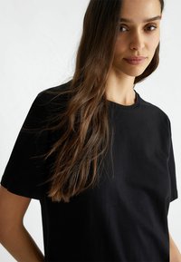 T-shirt in cotone nero con maniche corte, scollatura rotonda e una texture liscia, caratterizzato da un taglio rilassato e un design semplice.