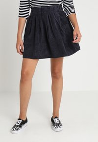 Falda de pana en azul oscuro con pliegues y una cinturilla elástica, combinada con zapatillas negras con un patrón de cuadros blanco y negro.