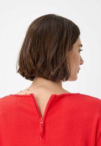 Maglione rosso con scollatura rotonda e chiusura con zip sul retro. Tessuto dalla texture liscia e silhouette aderente.