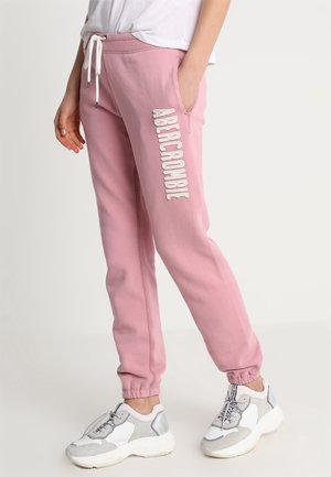 Person iført lyserøde joggingbukser med "ABERCROMBIE" i hvide bogstaver på benet, hvid snøre og hvide sneakers med grå accenter.