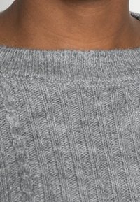 Maglione grigio lavorato a maglia con una texture a costine. Presenta un collo tondo e un giogo orizzontale, che mette in mostra dettagli in treccia intricati.