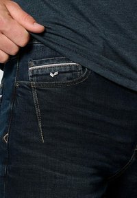 Tmavě modré džíny z denimu s tradičním pětikapsovým designem, s malým kovovým logem na přední kapse a viditelnými švy.