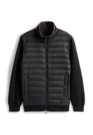 Črna jakna s prešitim sprednjim delom, mehkimi pletenimi rokavi, stoječim ovratnikom in dvema sprednjima žepoma z zadrgo. Na prsih je diskreten logotip.