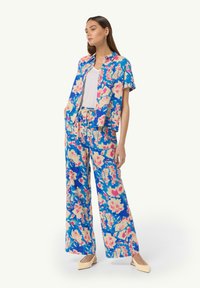 Zweiteiliges Outfit mit Blumenmuster in Blau, Pink und Beige; Kurzarmhemd mit offenem Kragen, weite Hose mit Kordelzugbund.