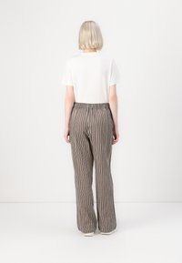 Prúžkové nohavice v béžovej a hnedej farbe s elastickým pásom. Model má na sebe obyčajné biele tričko, pohľad zozadu.