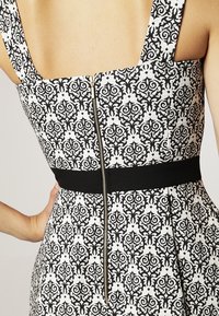 Abito a righe in bianco e nero con scollatura quadrata, zip a vista sul retro e una cintura nera solida. Tessuto dalla trama liscia.