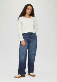 Witte lange mouwen top gecombineerd met donkerblauwe wijde spijkerbroek. De jeans hebben een klassiek ontwerp met vijf zakken en eenvoudige stiksels. Lichte sneakers maken de outfit compleet.
