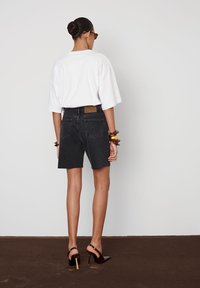 Mustad denimi šortsid, millel on kulunud serv, kõrge vöökoht ja tagataskud, koos laia valge T-särgi ja rihmadega kõrge kontsaga kingadega.