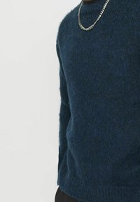 Granatowy sweter wykonany z miękkiej, teksturowanej tkaniny, o klasycznym okrągłym dekolcie i luźnym fasonie, podkreślony srebrnym naszyjnikiem.