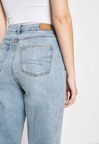 Vaaleansiniset farkut, joissa on korkea vyötärö, takataskut ja ruskea nahkainen etiketti vyötäröllä. Sileä pinta.