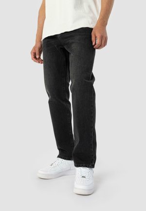 Black denim jeans with a slim fit, featuring subtle whiskering and five-pocket design. Paired with white sneakers.