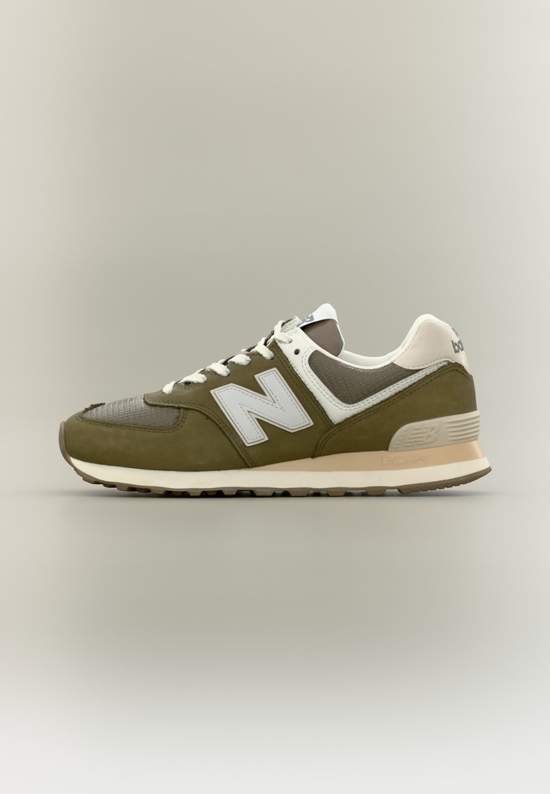 Olijfgroene en beige New Balance-sneaker met wit logo en veters, bovenwerk van mesh en suède, geplaatst op een eenvoudige lichte achtergrond.