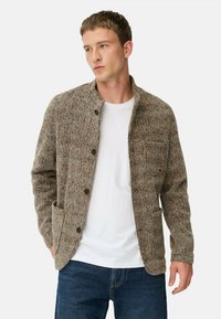 Brauner, strukturierter Strickcardigan mit Knopfleiste, breitem Kragen, einer Brusttasche und zwei Seitentaschen, getragen über einem weißen T-Shirt.