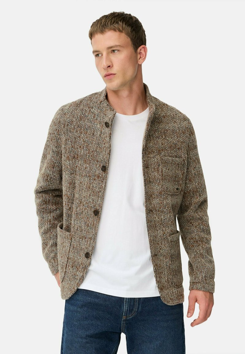Brauner, strukturierter Strickcardigan mit Knopfleiste, breitem Kragen, einer Brusttasche und zwei Seitentaschen, getragen über einem weißen T-Shirt.
