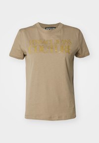 Beige katoenen t-shirt met grote gouden glitters tekst "VERSACE JEANS COUTURE" over de voorkant. Klassieke ronde hals en korte mouwen.