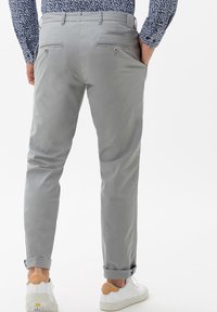 Chinos grigio chiaro con vestibilità slim, dotati di due tasche posteriori con chiusura a bottone e orli arrotolati. Indossati con sneakers bianche.