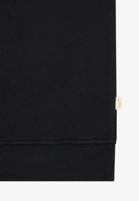 Svart hettegenser med myk tekstur, ribbestrikkede mansjetter og en liten beige etikett på kanten. Enkelt design, ingen ekstra mønstre eller detaljer.