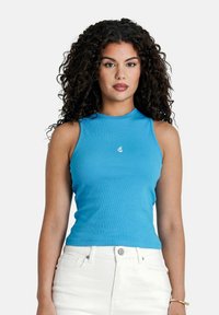 Top in cotone ribbed blu chiaro con collo alto e senza maniche, dotato di un piccolo logo sul petto. Abbinato a pantaloni bianchi a vita alta.