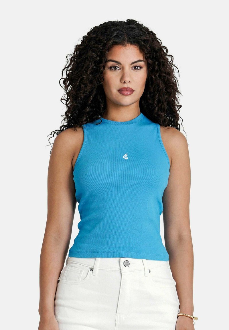 Top in cotone ribbed blu chiaro con collo alto e senza maniche, dotato di un piccolo logo sul petto. Abbinato a pantaloni bianchi a vita alta.