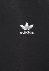 Vêtements de sport noirs en tissu texturé avec un logo adidas blanc proéminent et trois rayures parallèles au-dessus.