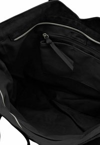 Intérieur d'un sac fourre-tout en tissu noir, avec un compartiment zippé, une texture lisse et une petite poche attachée avec une sangle.